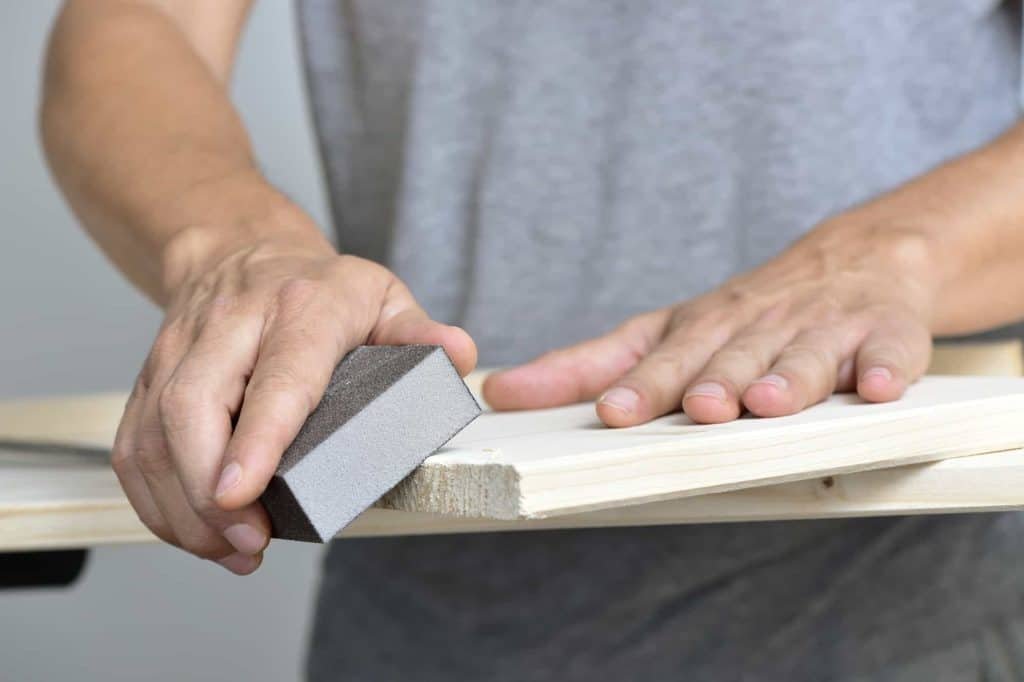 man sanding a wooden board with a sanding block