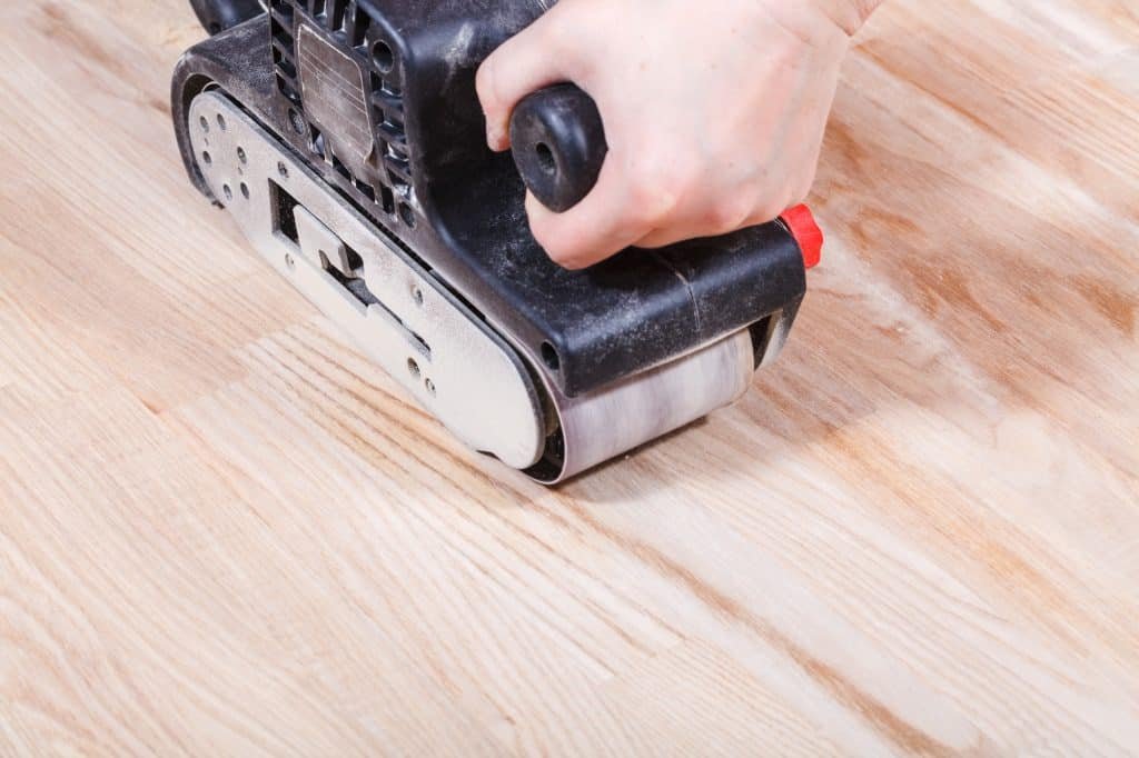 sanding a wooden floor by a hand-held belt sander