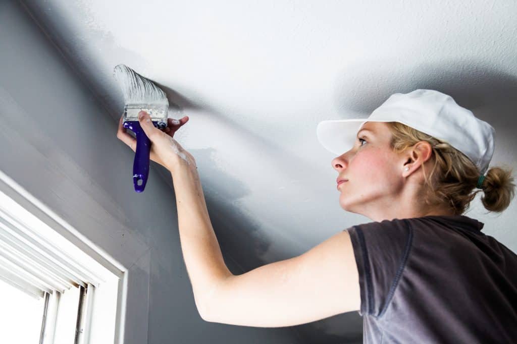 woman painting the edges of the ceiling using a brush