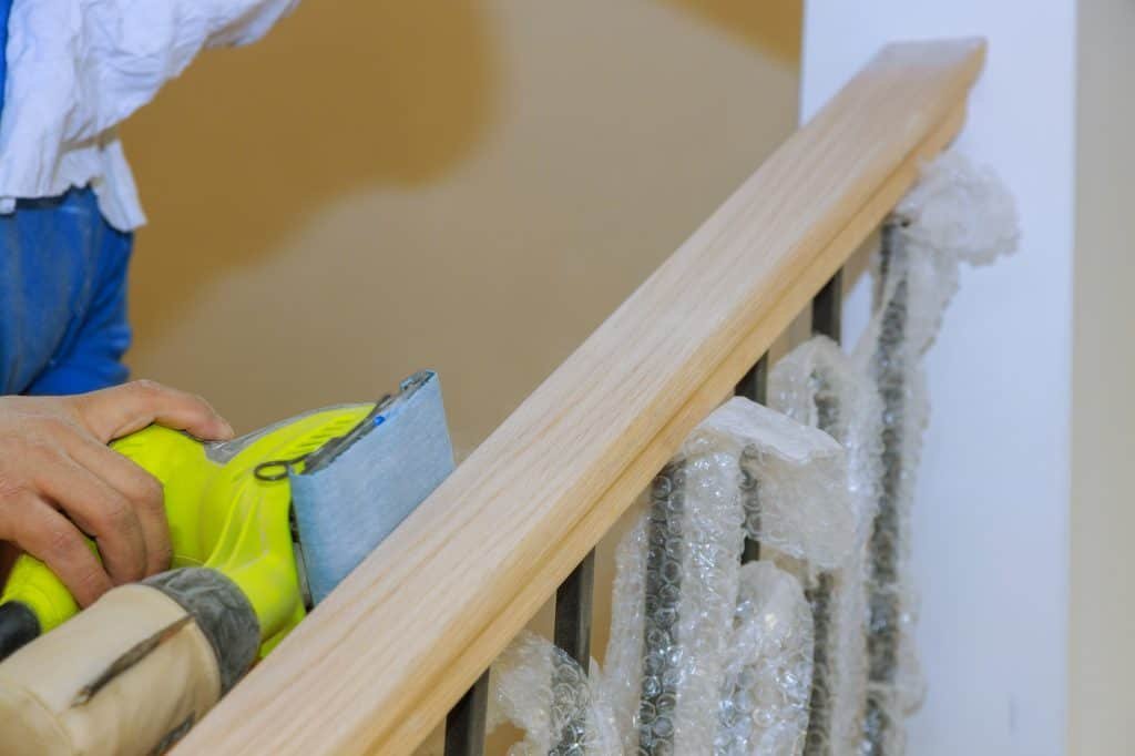 man sanding a wooden stair railing