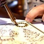 an artist using a soldering iron to burn wood