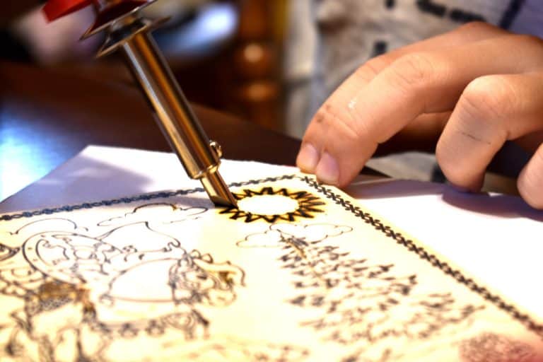 an artist using a soldering iron to burn wood