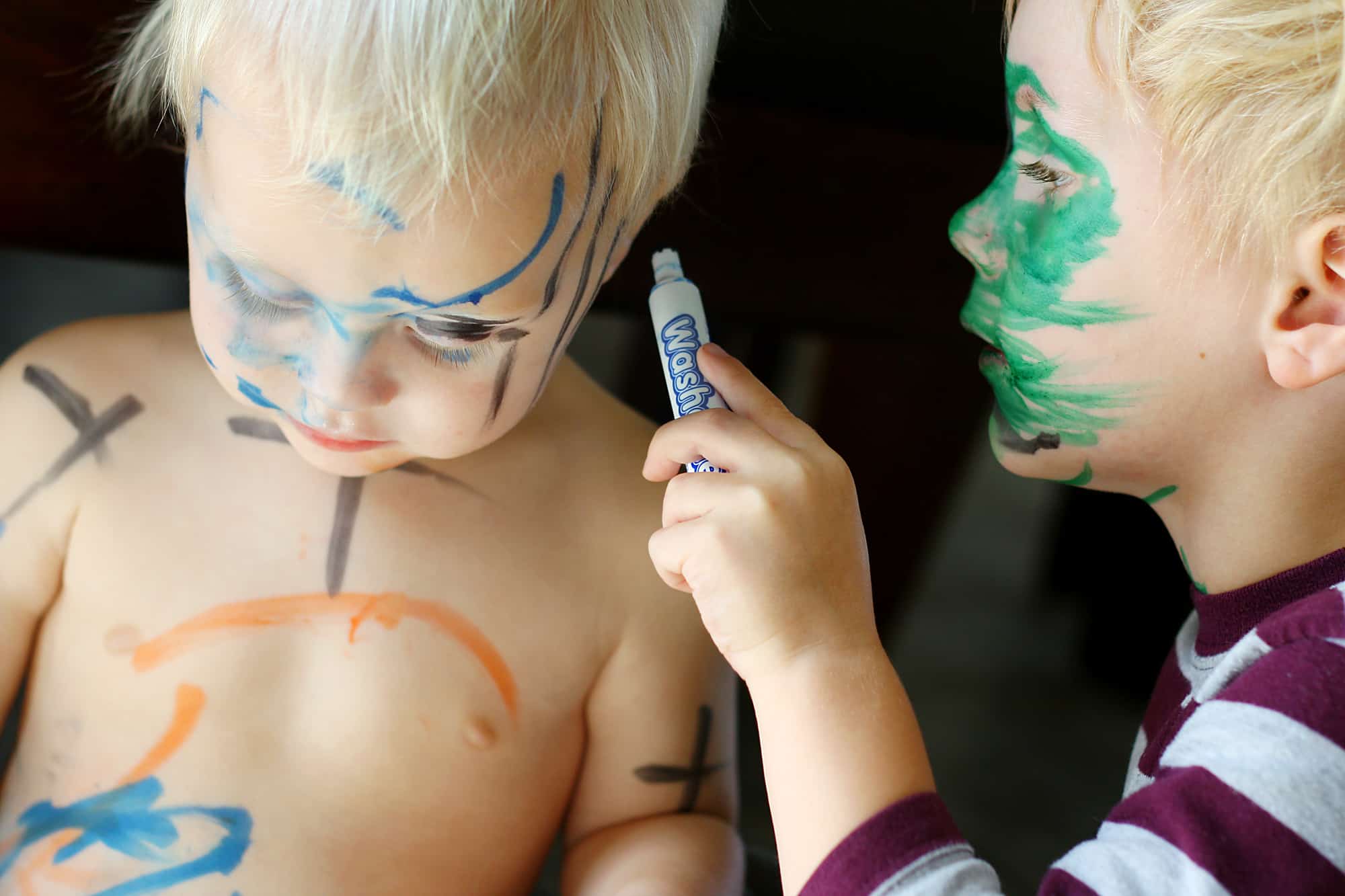 young child use washable marker to draw on his brother's skin